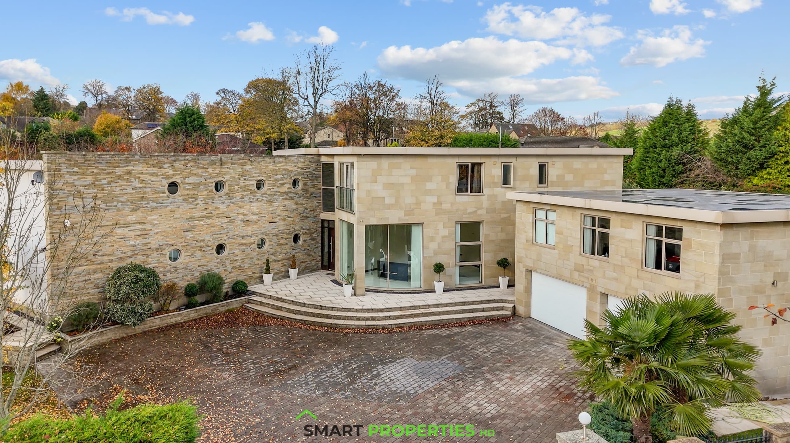 Contemporary stone house with a curved glazed entrance, porthole windows along the boundary wall and a block-paved drive.