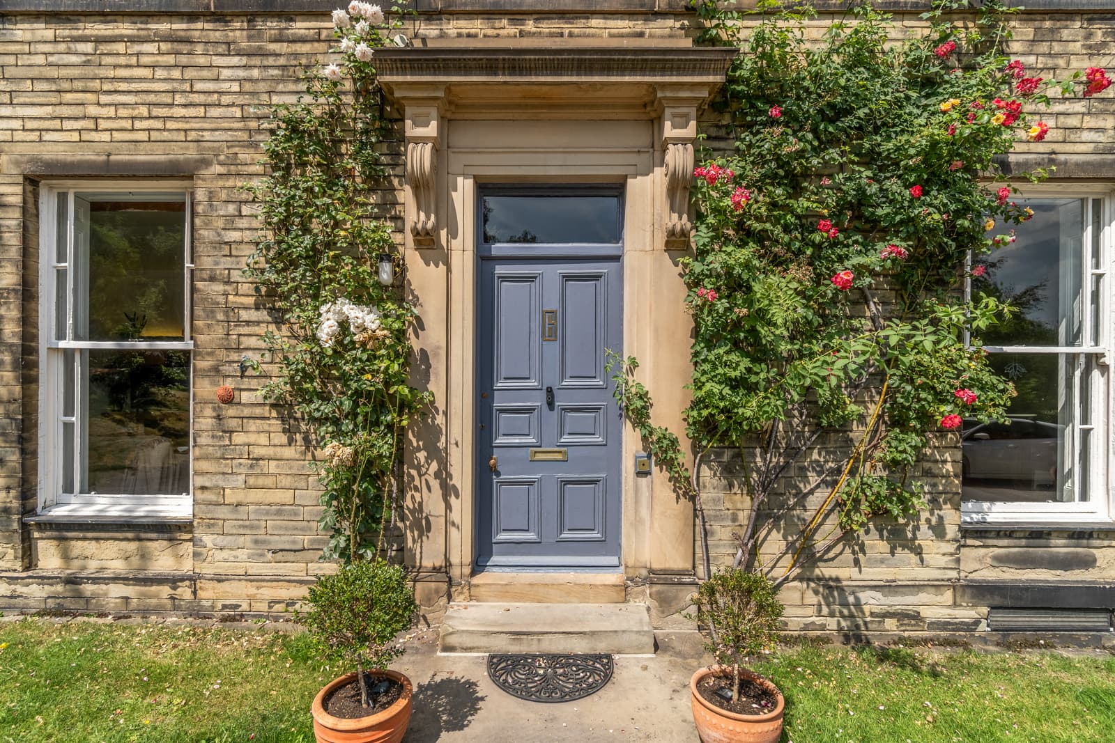 Slate-blue front door in a carved stone surround, climbing roses in flower up the sash-windowed frontage.